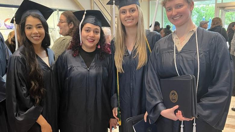 四名毕业生在毕业典礼上戴着帽子，穿着礼服摆姿势拍照